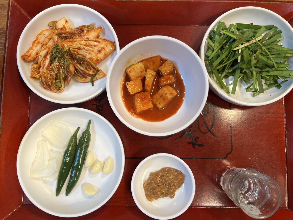 デジクッパと一緒に並ぶ釜山の食堂の副菜。キムチ、カクトゥギ、ニラの和え物が静かに食卓を整える。