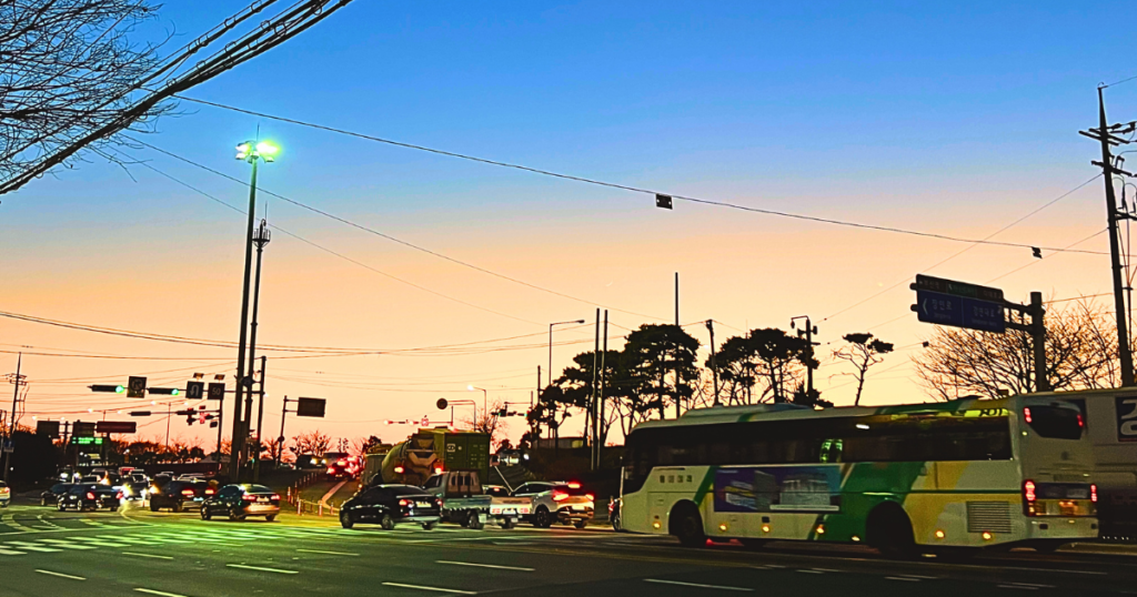 釜山の夕暮れ時。鮮やかな空の色と車道を列を作って走る移動中の車の対比が美しい生活の風景